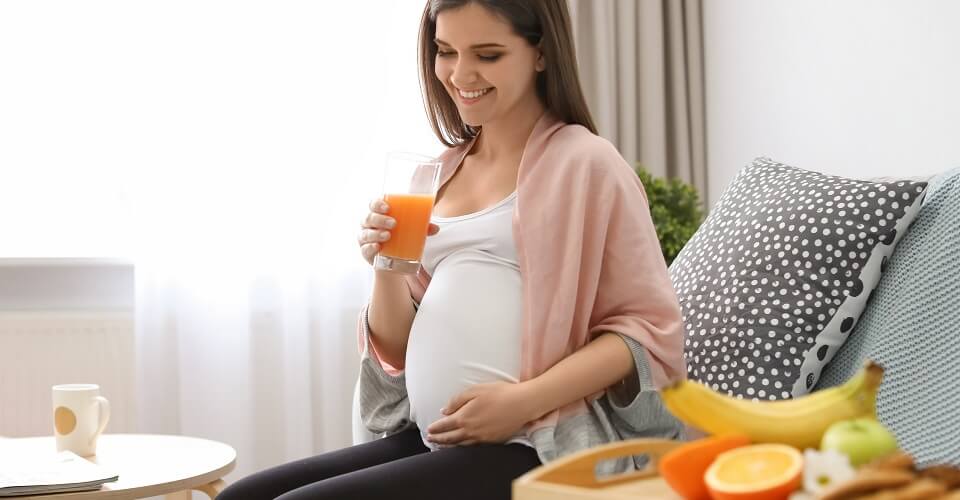 A pregnant woman drinks juice next to a fruit